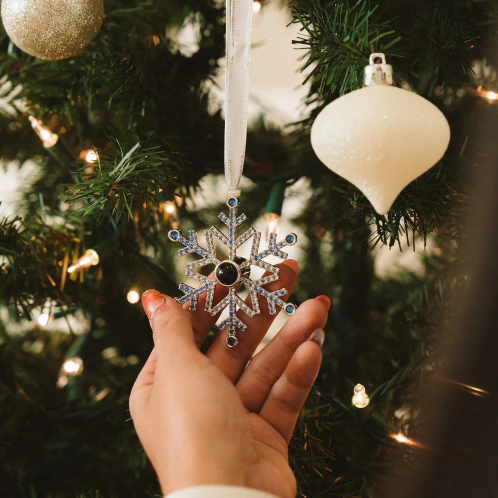 Hand holding a silver snowflake ornament in front of a decorated Christmas tree.